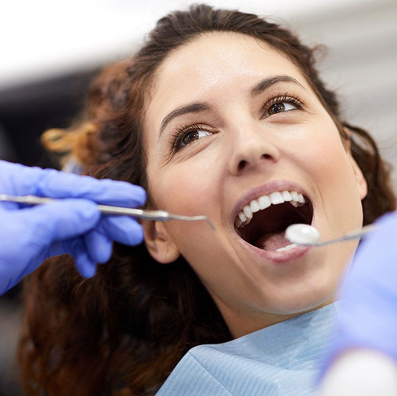 Dentist examining a smiling patient’s teeth with a mirror