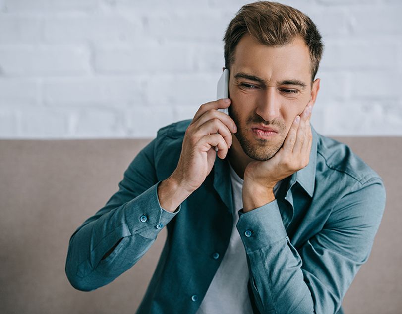Man holding his cheek in pain while calling the dentist